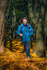 Outdoor adventurer with beard in a blue jacket enjoying a peaceful autumn hike among tall trees and...