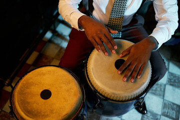 Cropped shot of male musician wearing suit with tie playing beat on traditional conga drums, while...