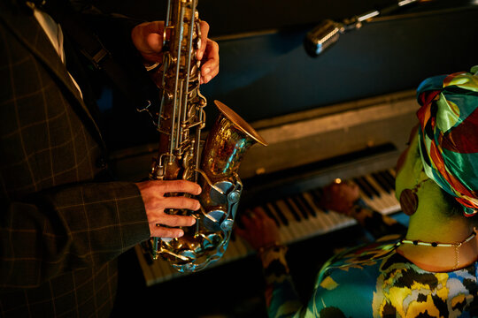 Cropped shot of multiracial musicians improvising on saxophone and piano during jam session in jazz club