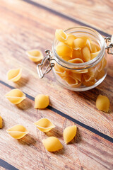 Raw uncooked dried Conchiglie shell pasta. Italian seashells pasta in lock lid jar on wooden background.