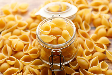 Raw uncooked dried Conchiglie shell pasta. Italian seashells pasta in lock lid jar on wooden background.