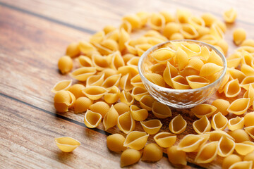 Raw uncooked dried Conchiglie shell pasta. Italian seashells pasta in glass bowl on wooden background.
