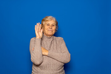 Hello concept. A happy, smiling, elderly Caucasian woman in her 70s waves with her hand outstretched. Isolated on a blue studio background.