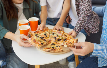 Close-up shot of a parents with two children in family setting eating fast food pizza for lunch together at home living room, enjoying leisure in a cozy environment with joy and connection.
