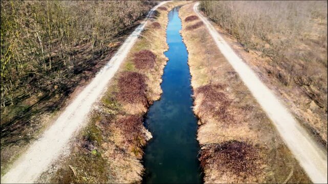 Drone flight along a straight section of the Orco Stream in Montanaro, Italy. Lush plants and calm water create a scenic and peaceful natural view. Ideal for nature and travel projects.