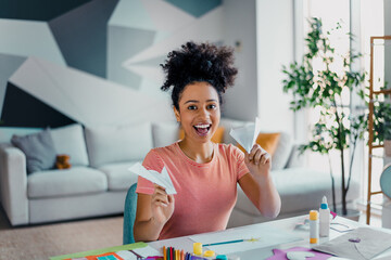 Happy young woman holding paper crafts in a cozy modern living room with bright interior and...