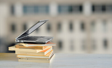 Laptop computer and stack of books ,blurred office building as background.Beat the clock,office...