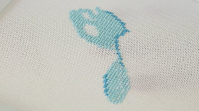 Close-up of partially completed cross-stitch embroidery, intricate light blue threads on a beige background of fabric emphasizing the art of needlework