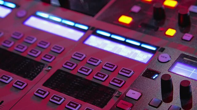 A close-up of digital audio mixer featuring illuminated buttons and sliders in dynamic red and blue lighting, creating a vibrant atmosphere for music production