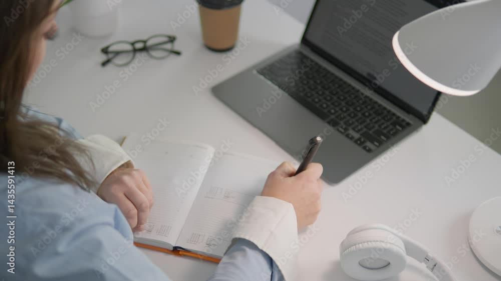 Poster a dedicated individual writes in a notebook and works on a sleek laptop, showcasing productivity and