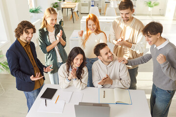 Group of happy university students celebrating successful collaboration in modern classroom. Joyful young people clapping hands, congratulating each other with productive teamwork. Education concept.