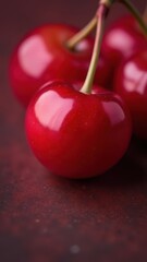 A close-up of a vibrant red cherry tomato with glistening skin on a soft-focus maroon background
