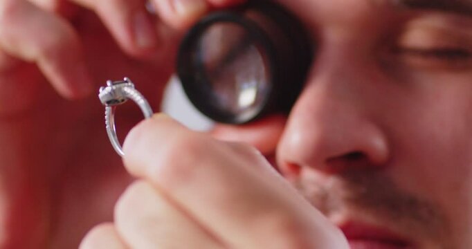 Jeweler meticulously evaluates ring through magnifying glass, demonstrating attention to detail. Close up of a ring in hand of professional jeweler who makes or repairs luxury rings. 4K video.