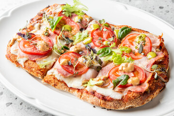 A delicious flatbread pizza topped with fresh tomatoes, greens, and savory ingredients, arranged beautifully on a white plate, perfect for showcasing casual dining and Italian cuisine.