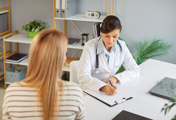 Fototapeta premium Young woman patient talking to female doctor in office during medical examination. Woman physician listening to the patient's complaints in clinic. Healthcare and medicine concept.