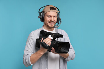 Man with professional video camera and headset on light blue background