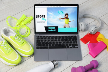 Laptop with sport blog web site and different gym stuff on floor, above view