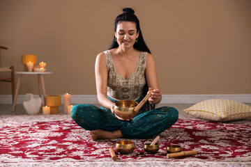Woman with singing bowls and burning candles indoors