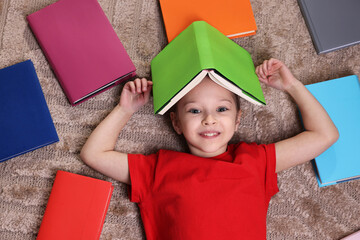 Cute girl with many different books on rug at home, top view