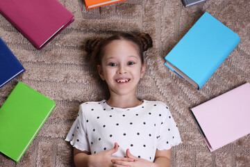 Cute girl with many different books on rug at home, top view