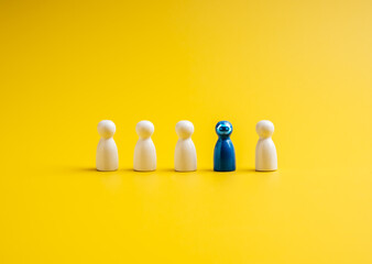 The blue one with robot face, different standing out of the group of white peg dolls, people symbols, isolated on yellow background. Artificial Intelligence jobs, AI robot career, recruitment concept.