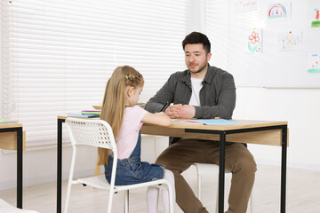Teacher having lesson with little girl at desk indoors