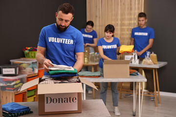 Group of volunteers packing donation goods at tables indoors, selective focus