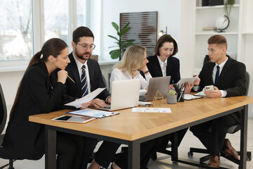 Coworkers with different devices working together at wooden table in office