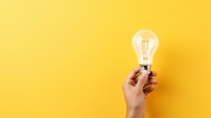 Hand holding pencil drawing a light bulb on yellow background, with clear space for text placement.

