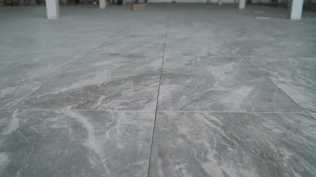Workers are installing large gray marble tiles in a spacious, modern building under construction