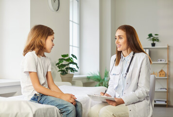 Obraz premium Friendly female child doctor pediatrician giving consultation and talking with little boy patient sitting on couch in medical clinic in exam room during checkup. Pediatrics and medicine concept