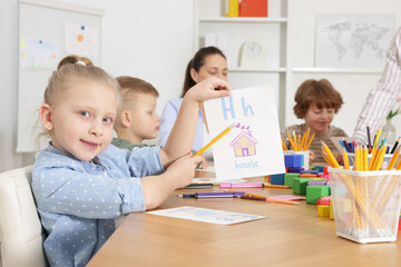 Fototapeta premium Cute girl showing card with letter H during lesson in school