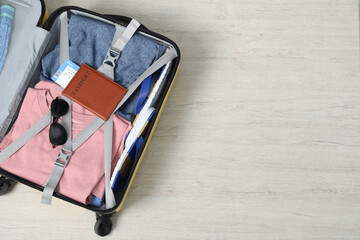 Different clothes, passport and sunglasses in open suitcase on light wooden floor, top view. Space...