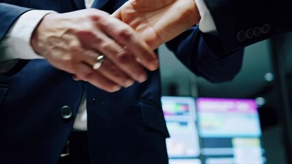 Businesspeople shaking hands in office with stock market data screens - Powered by Adobe