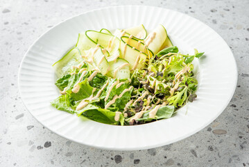 A fresh salad featuring mixed greens and sliced zucchini, drizzled with a light dressing, elegantly presented in a white bowl, perfect for showcasing healthy dining options.

