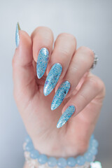 Female hand with long nails and bright light blue and silver manicure