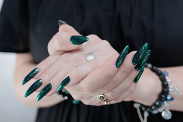 Woman's hand with long nails and black green nail polish