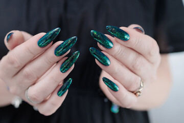 Woman's hand with long nails and black green nail polish