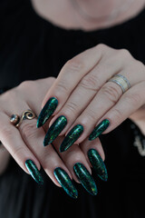 Woman's hand with long nails and black green nail polish