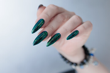 Woman's hand with long nails and green blue nail polish