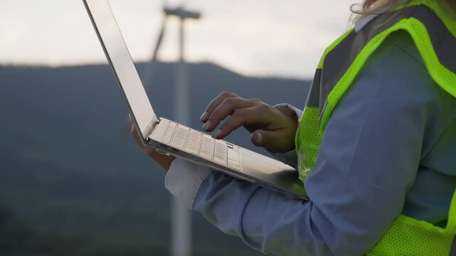 A skilled female engineer in a highvisibility vest analyzes data on her laptop among tall wind turbines, highlighting the blend of cuttingedge technology and renewable energy solutions