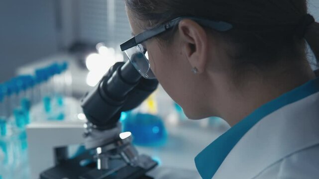 A passionate female scientist inspects samples with a microscope, surrounded by blue glassware and lab equipment, focusing on her groundbreaking research and innovations in biotechnology