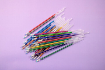 Multicolored ballpoint pens and ink refills on purple background stationery
