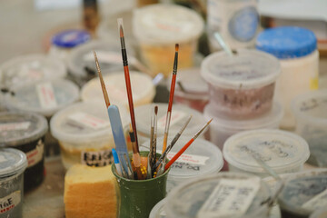 Art brushes in a ceramic holder with labelled paint jars create a creative atmosphere