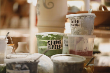 Pottery glaze containers labelled with colours on a shelf in a ceramics studio
