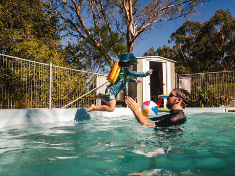 Toddler kid leaping into dads arms in backyard pool with childlike trust