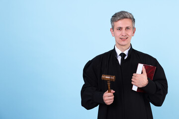 Smiling judge with mallet and book on light blue background. Space for text