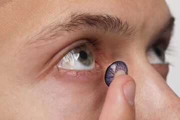 Man putting color contact lens in his eye, closeup