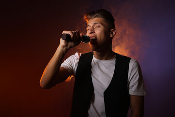 Talented young man singing on dark background with color light and smoke