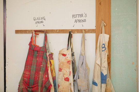 Colourful aprons on peg board in pottery workshop for glazing and pottery work